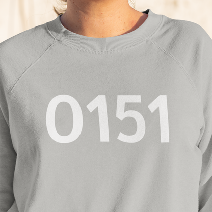 Close-up of a person wearing a light grey sweatshirt featuring the bold white “0151” design, photographed in natural daylight.
