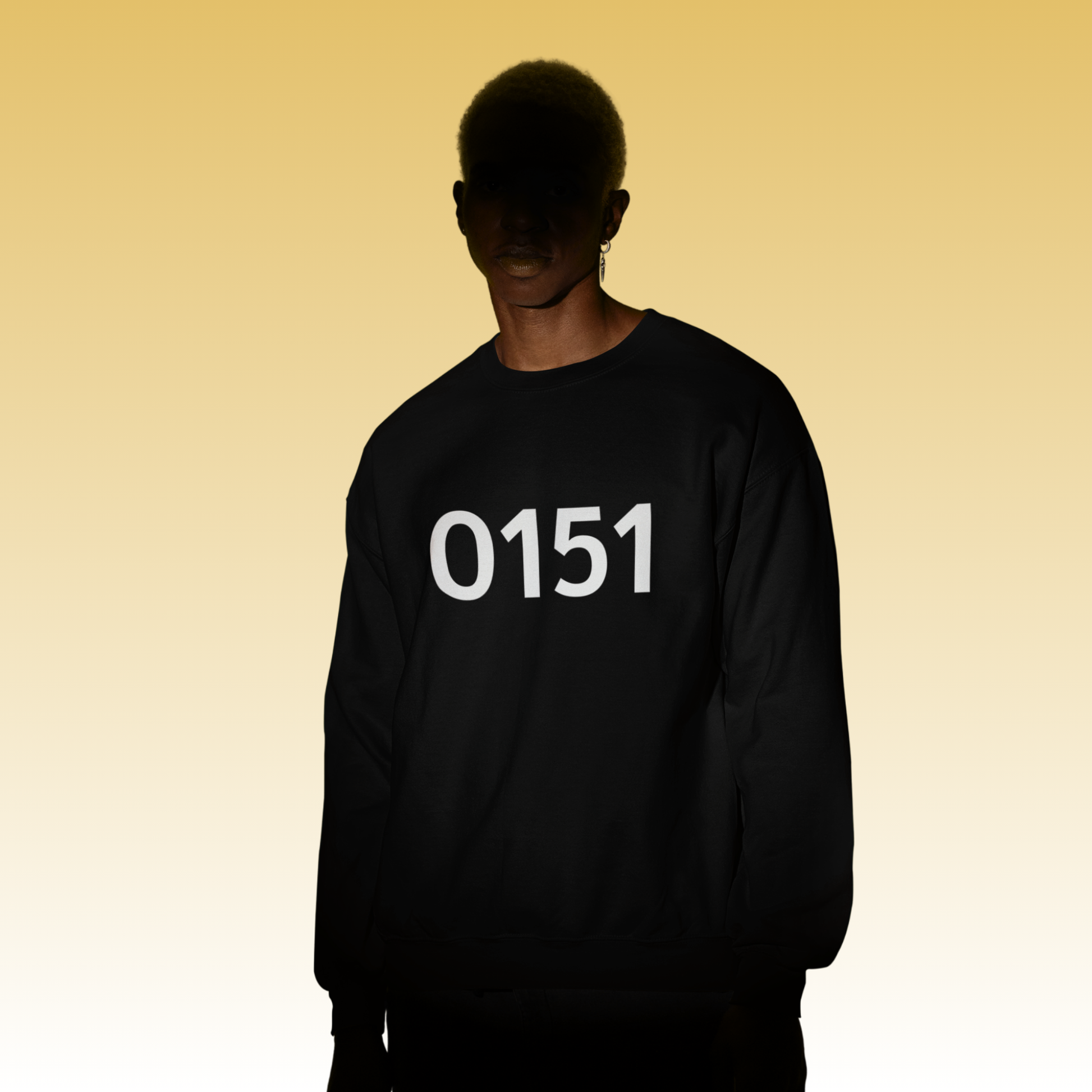Person wearing a black sweatshirt with large white “0151” print, standing against a golden gradient background.