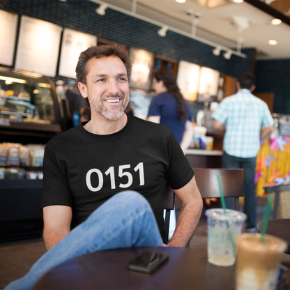 Man wearing a black “0151” t-shirt, sitting in a café with a coffee, smiling and relaxed.