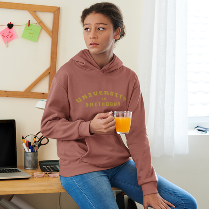 Young woman wearing a heritage brown “University of Smithdown” hoodie, sitting on a desk and holding a glass of orange juice, looking thoughtfully into the distance.